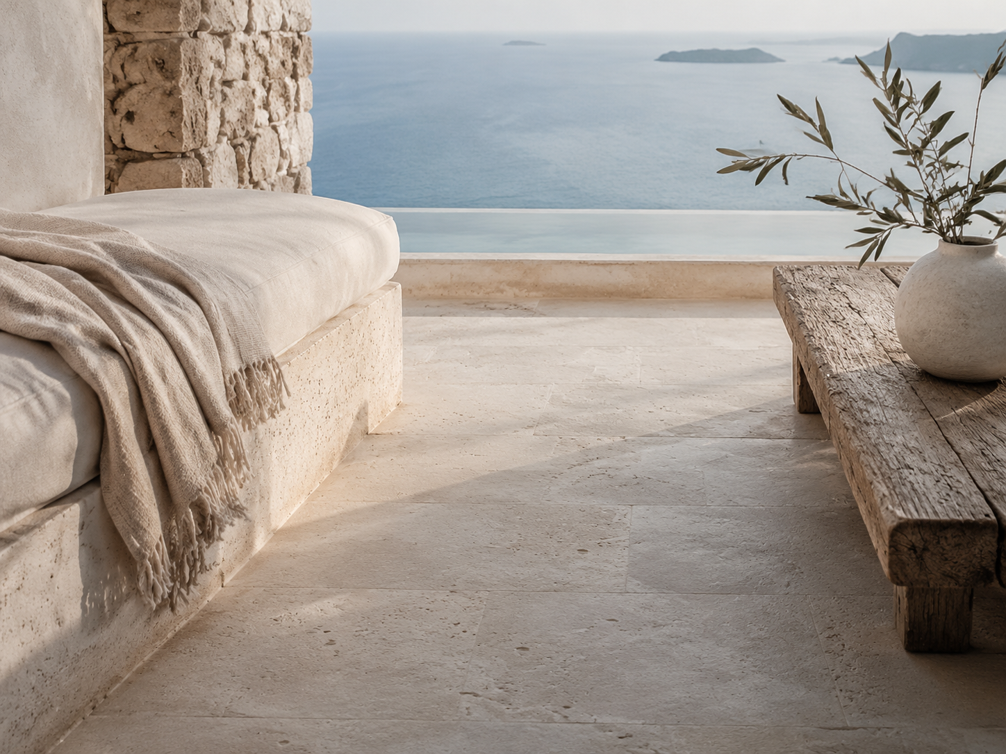 Warm limestone terrace with linen and an olive wood bench above the sea